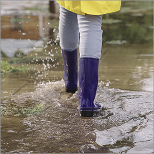 person in rain boots and yellow slicker walking through flooded area